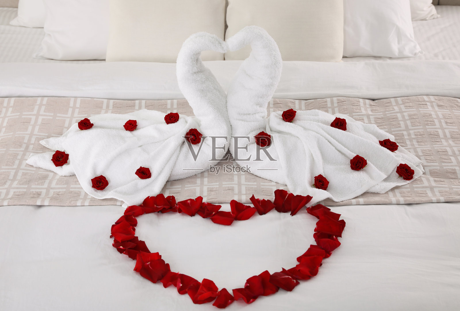 床上美丽的构图。用毛巾和玫瑰花瓣做成的天鹅呈心形照片摄影图片