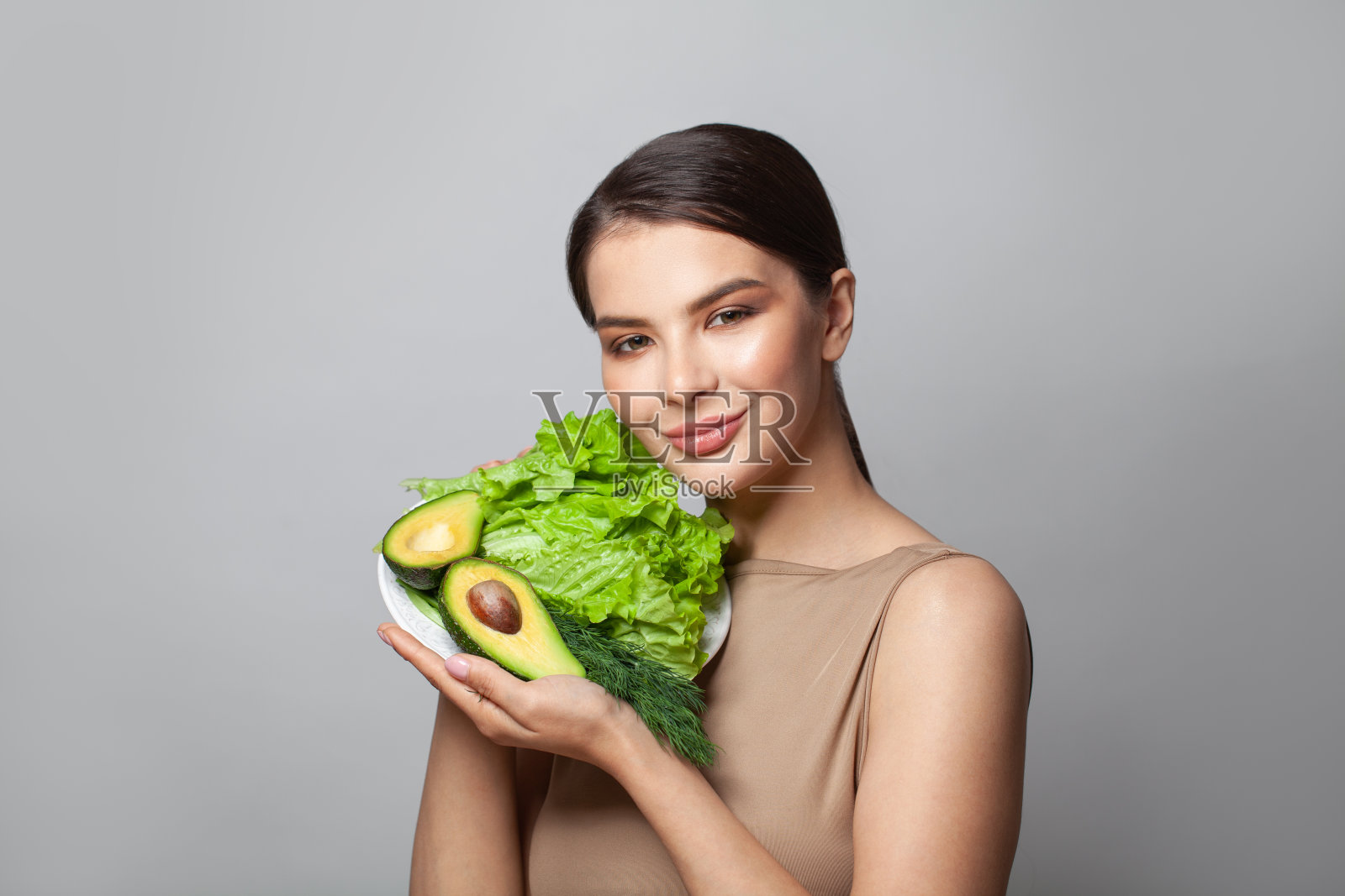 年轻女子的肖像显示鳄梨和绿色生菜在灰色的背景照片摄影图片
