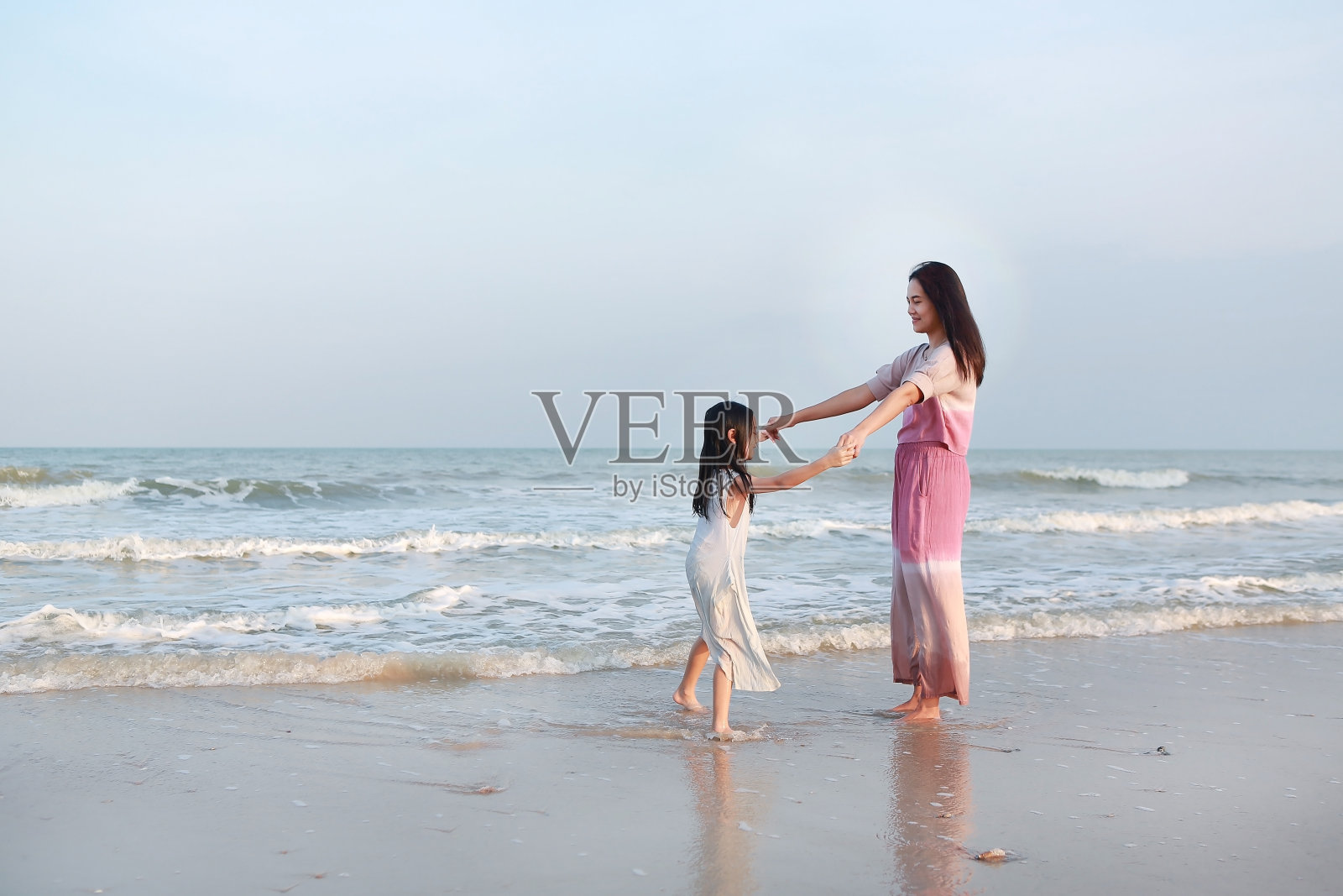 亚洲妈妈和女儿放松和一起跳舞的海滩度假时间。照片摄影图片