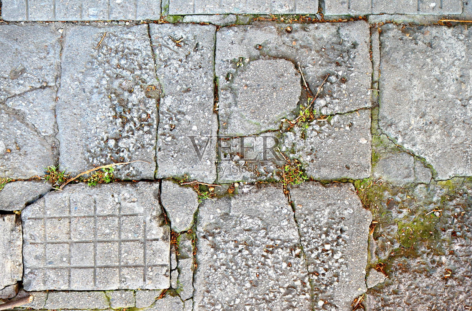 破碎的地板上有旧的裂缝的瓷砖，不规则的正方形之间有草-特写粗糙的纹理背景照片摄影图片