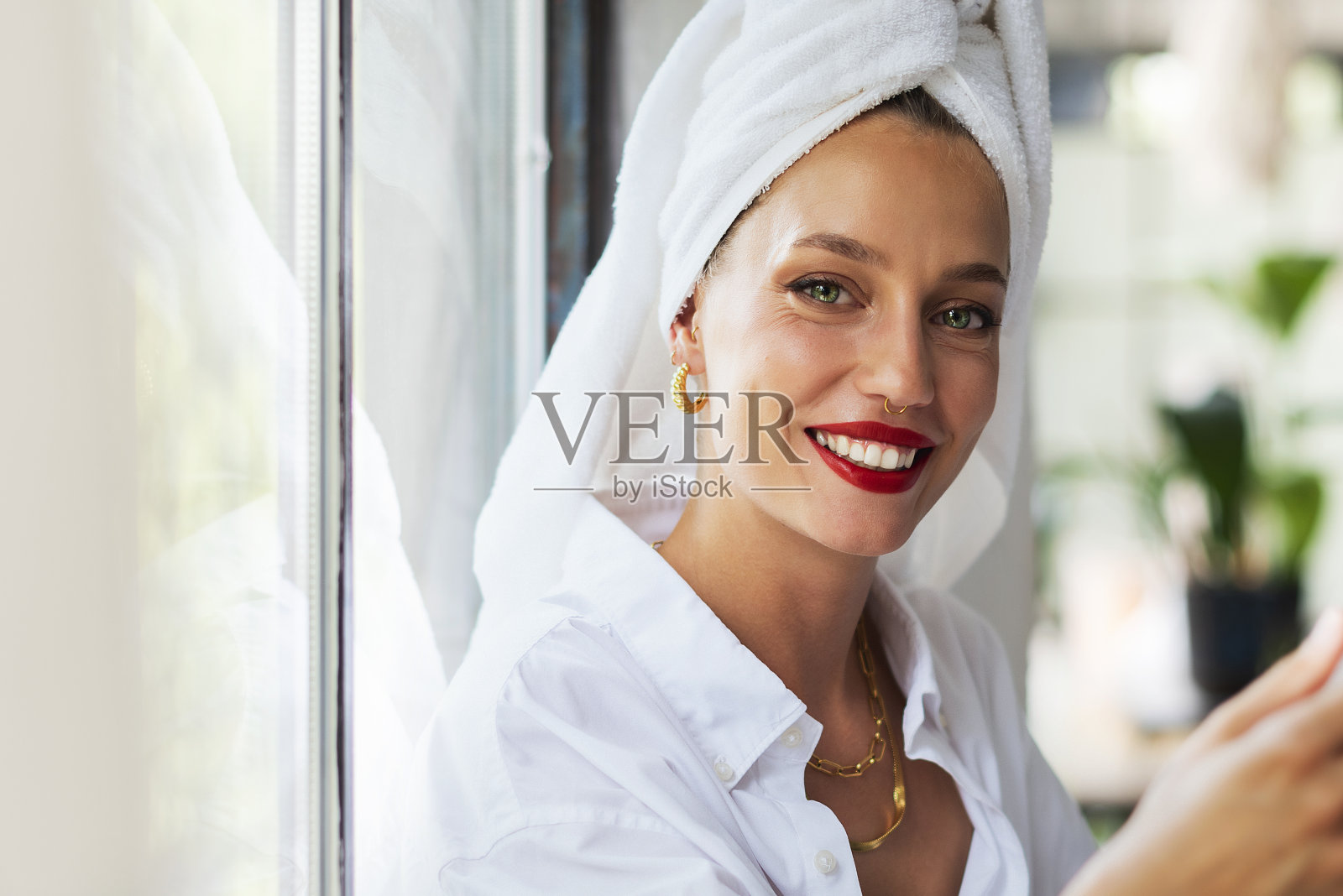 美丽的年轻女子涂着红色的口红，头戴头巾，在家里的窗口放松照片摄影图片