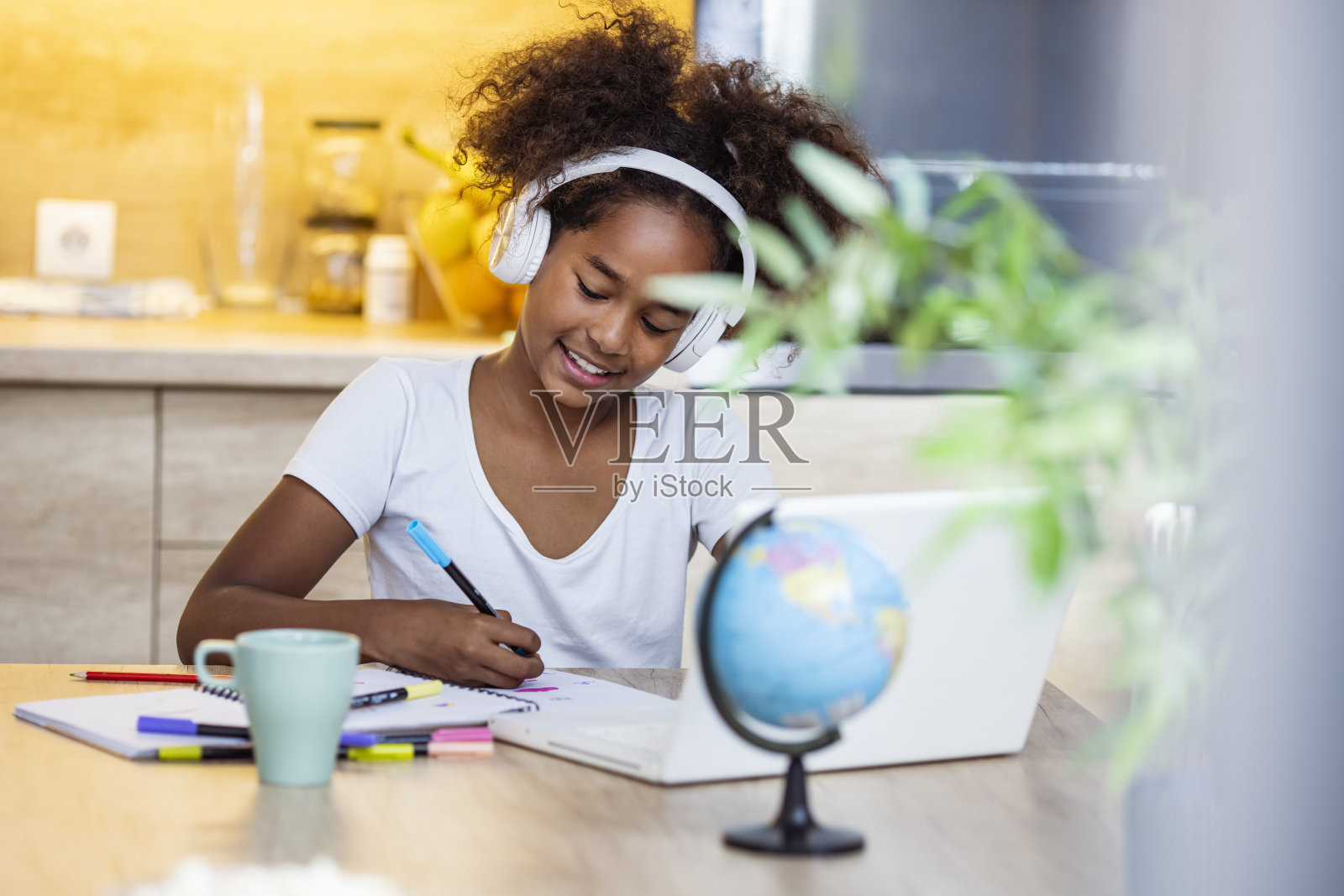 一个学龄前的小女孩戴着耳机坐在书桌前，用笔记本电脑在线学习照片摄影图片