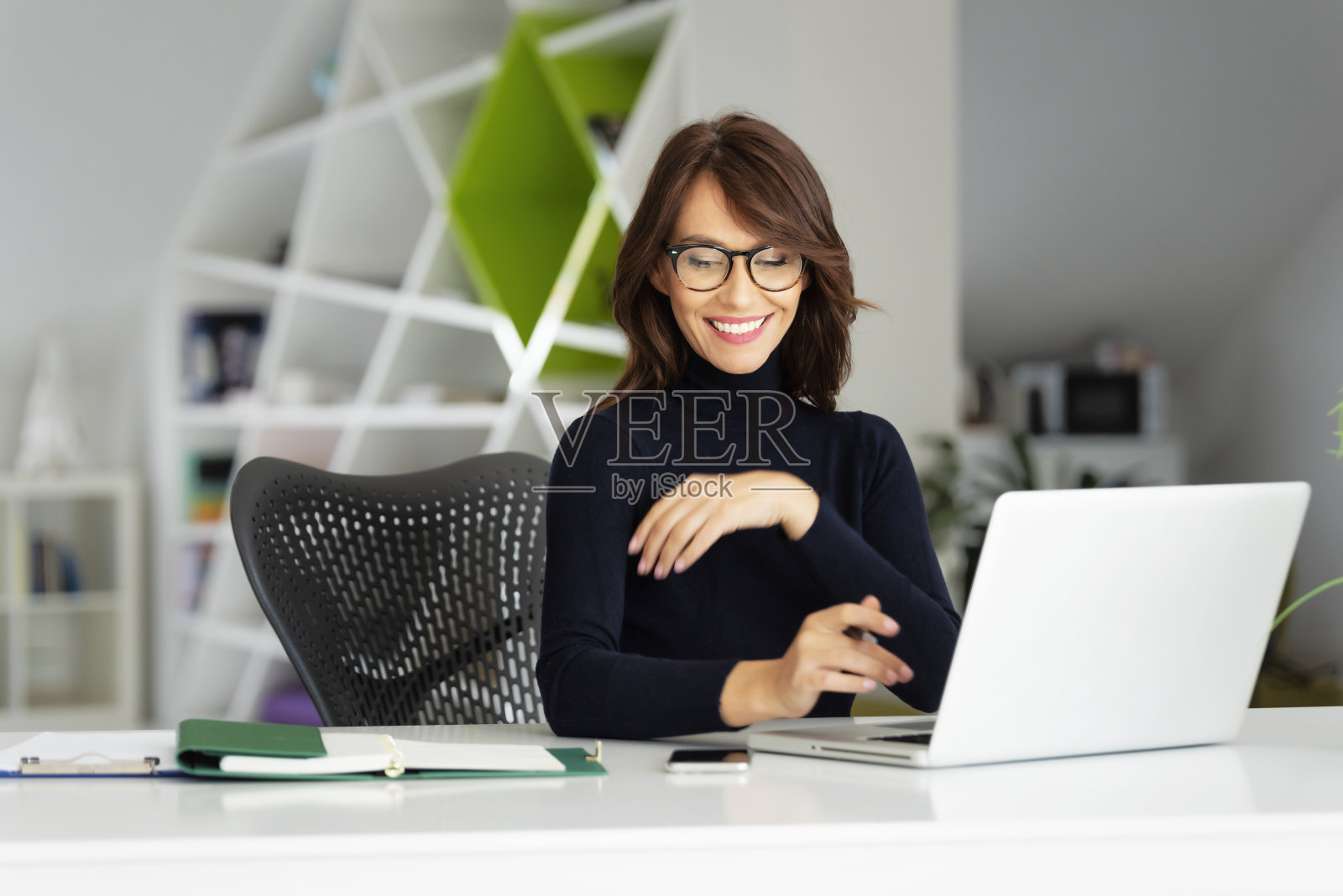 迷人的女商人穿着高领毛衣，在办公室用笔记本电脑工作照片摄影图片
