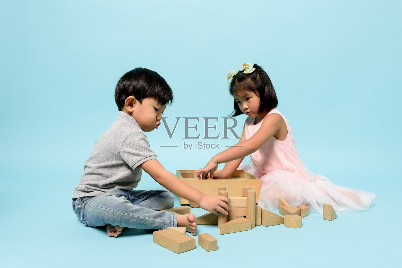 亚洲两个人的孩子一起玩的木头玩具块在淡蓝色背景的工作室。儿童技能，儿童角色与出生顺序，儿童发展概念。照片摄影图片
