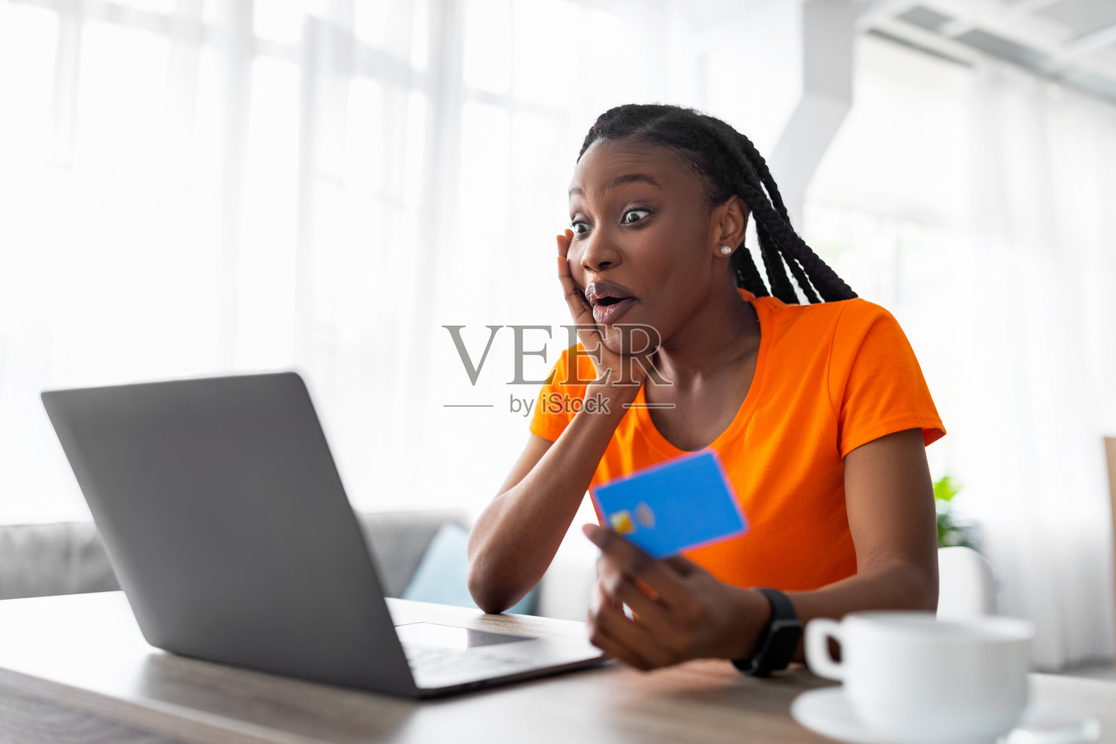 情绪激动的非洲女人看着笔记本电脑屏幕，拿着信用卡，震惊于网上商店的巨大销售照片摄影图片