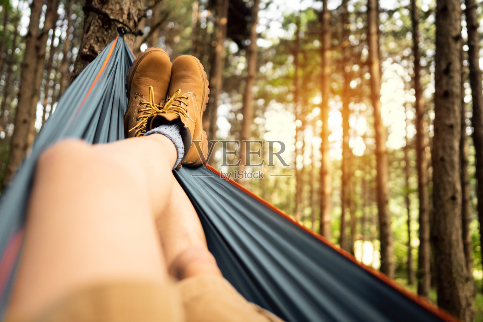 在松林里，一个穿着登山靴的陌生男子躺在吊床上休息照片摄影图片