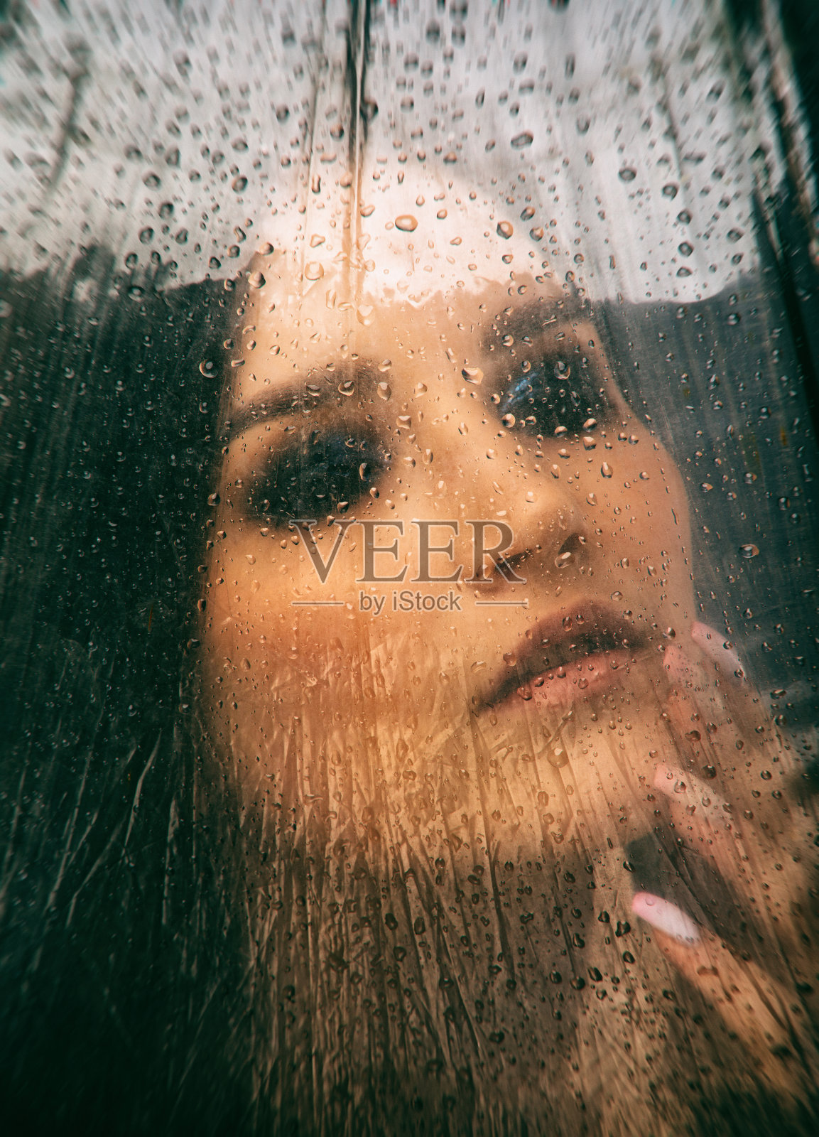 一个女孩坐在窗前，天气下着雨。窗户上可以看到雨点。照片摄影图片