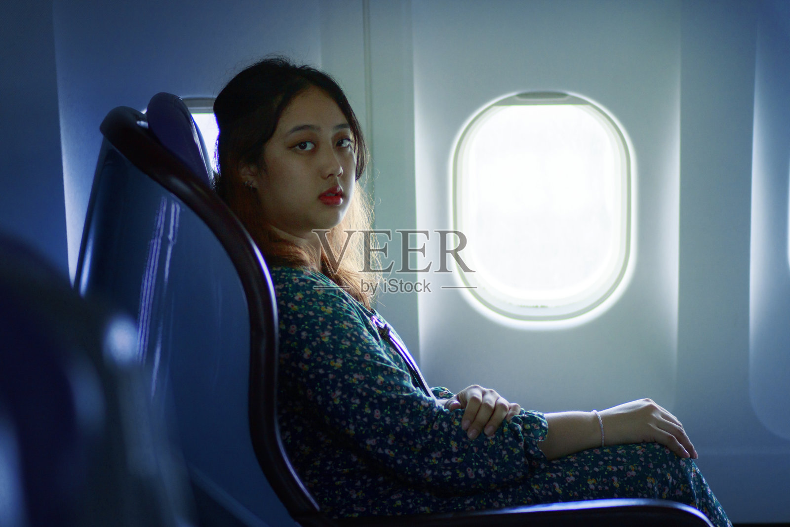 一位亚洲妇女坐在飞机窗旁的客舱座位上照片摄影图片