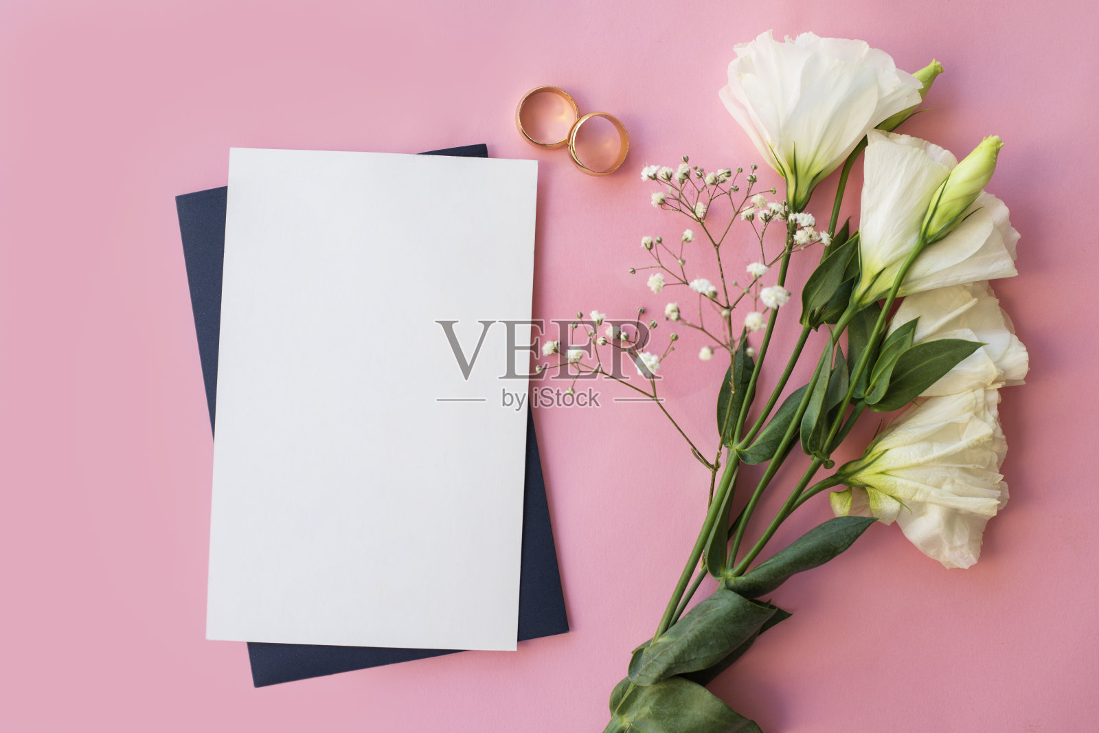 顶部视图与信封空卡片，鲜花和金色的结婚戒指在粉红色的背景照片摄影图片