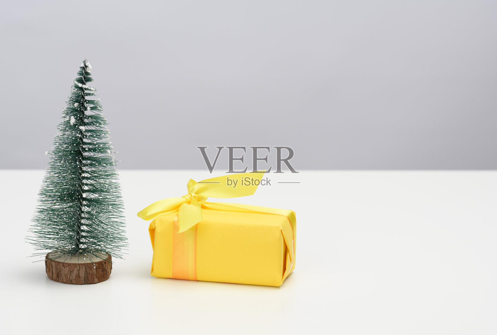 盒子用黄色的纸包裹着，白色的桌子上有一棵装饰性的圣诞树。节日的背景照片摄影图片