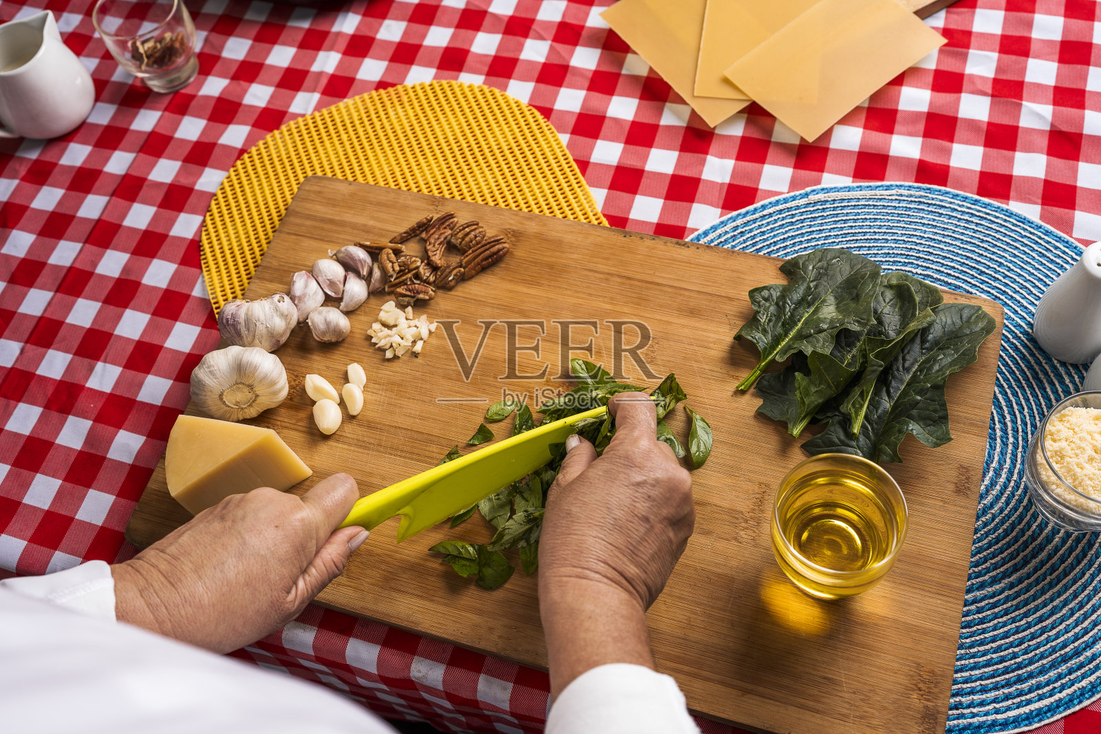 一个不知名的成年妇女在木制切菜板上用塑料刀切罗勒，准备制作香蒜酱。照片摄影图片
