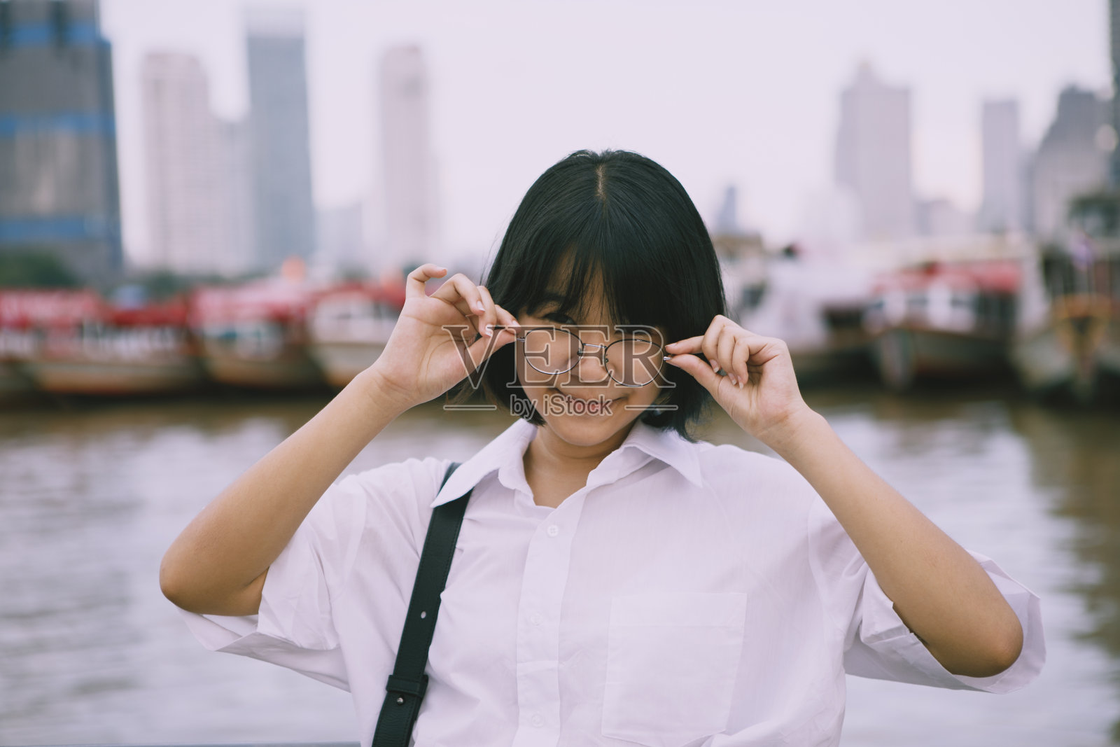 一个兴高采烈的亚洲少年戴着眼镜站在户外，背景是城市刮刀照片摄影图片