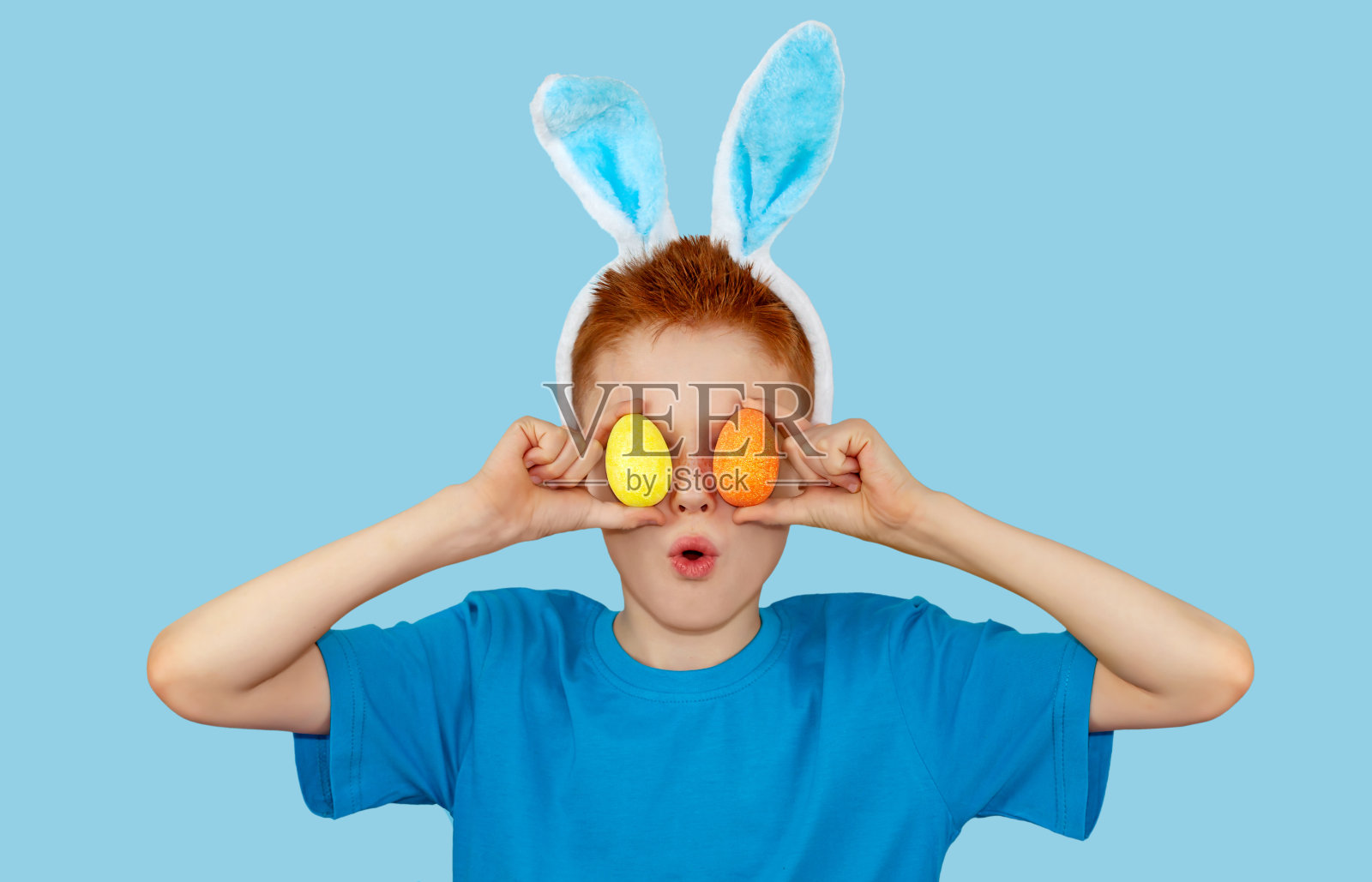 这是一个戴着兔子耳朵的红发男孩的肖像，他把五颜六色的复活节彩蛋举在眼前照片摄影图片